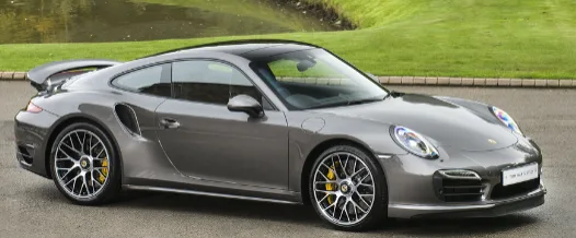 Grey Porsche 911 sports coupe parked in profile on a driveway beside a green lawn.