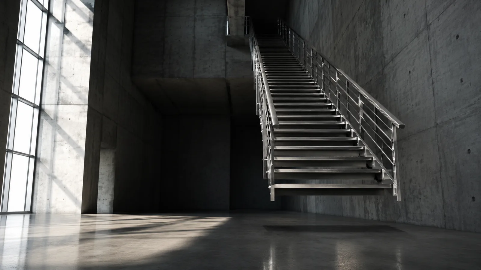 A modern steel staircase rising along a bare concrete wall in an empty, light-filled industrial space.