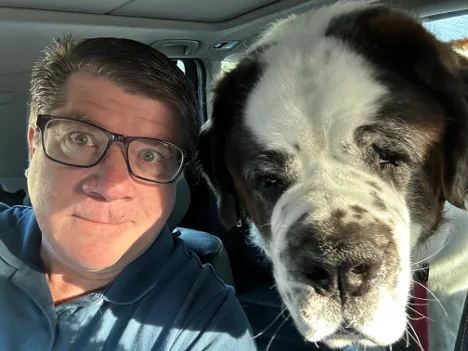 Man in glasses takes a car selfie beside a large Saint Bernard dog
