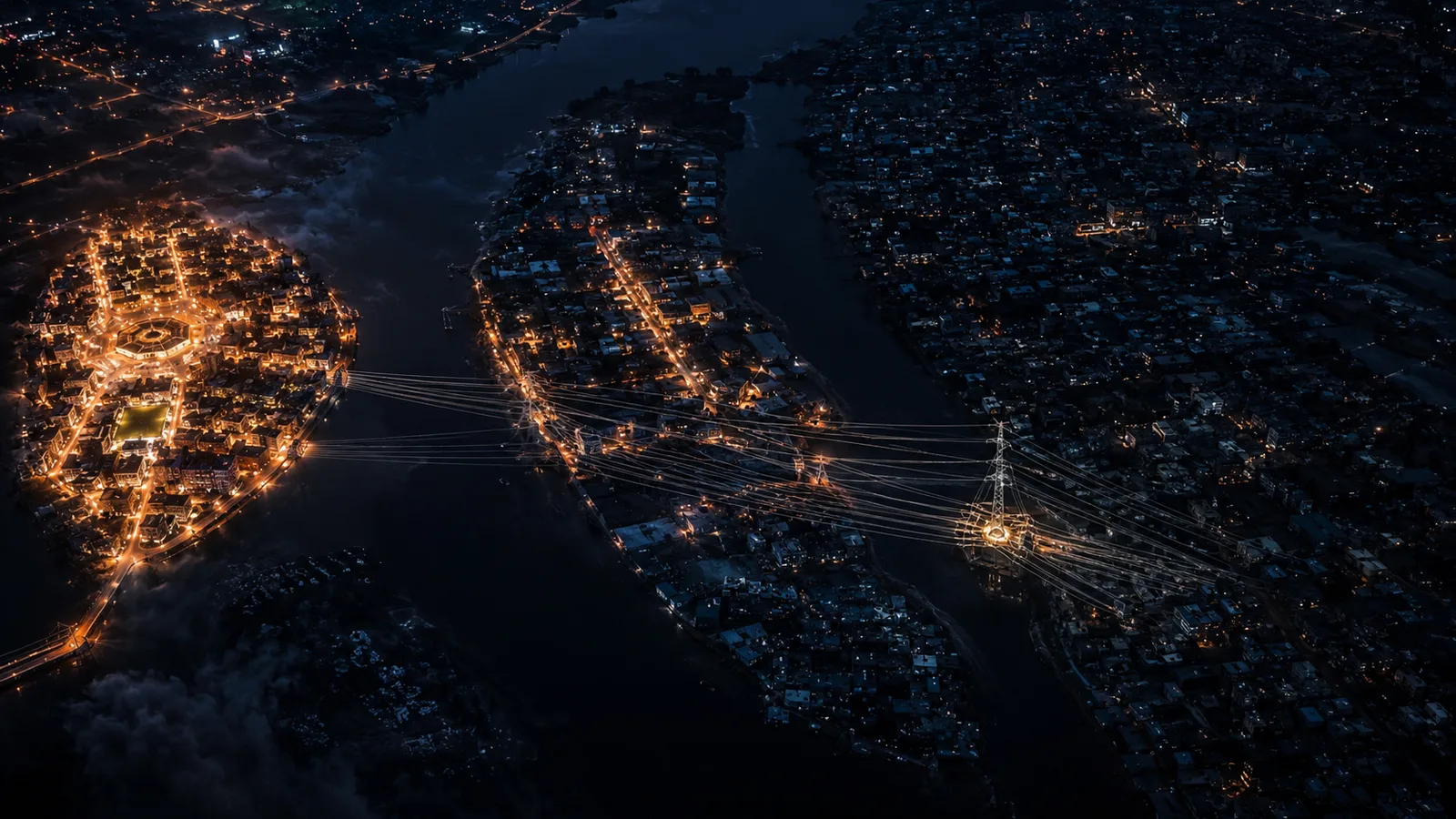 Aerial night view of a city divided by a dark river, its streets glowing gold with converging trails of light.