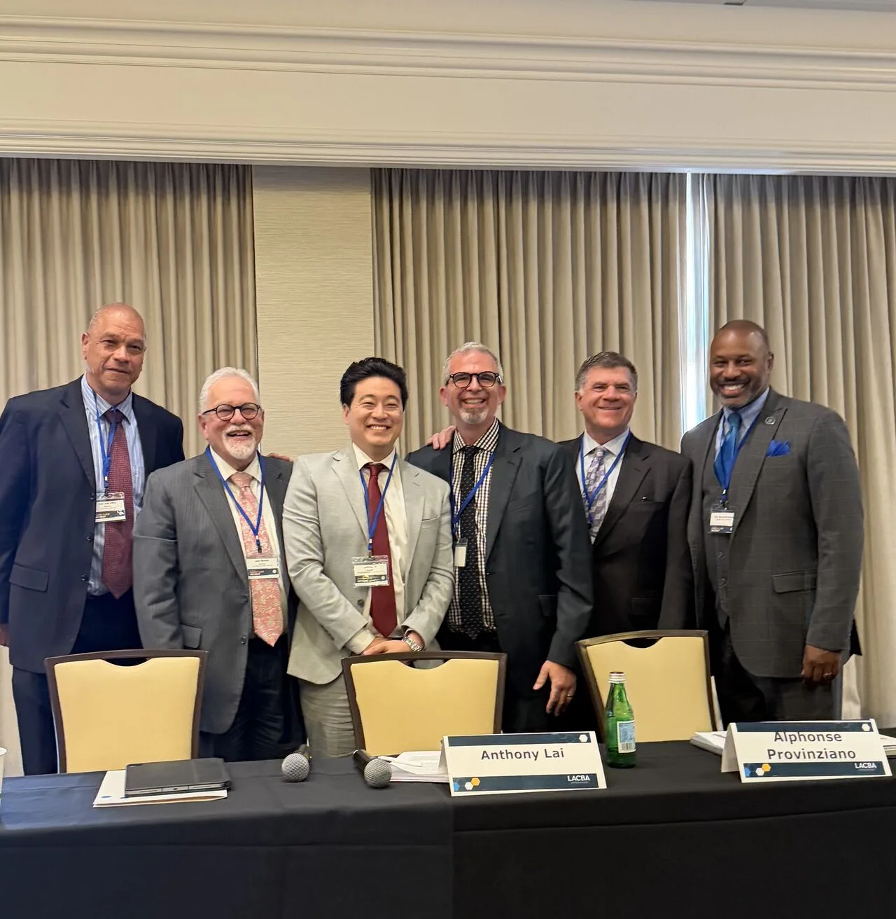 Six panelists in business attire standing together behind a table with name placards at a legal industry panel session.