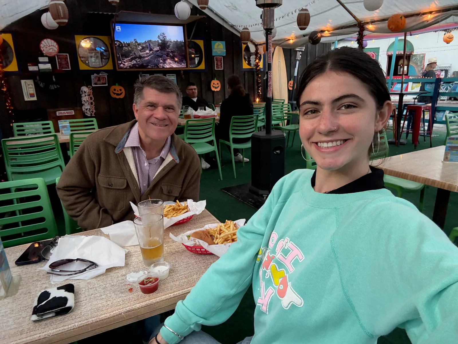 Steve and his daughter Charlotte smile for a selfie at a table with burgers and fries at The Shack, a casual burger place decorated with paper lanterns and Halloween pumpkins.