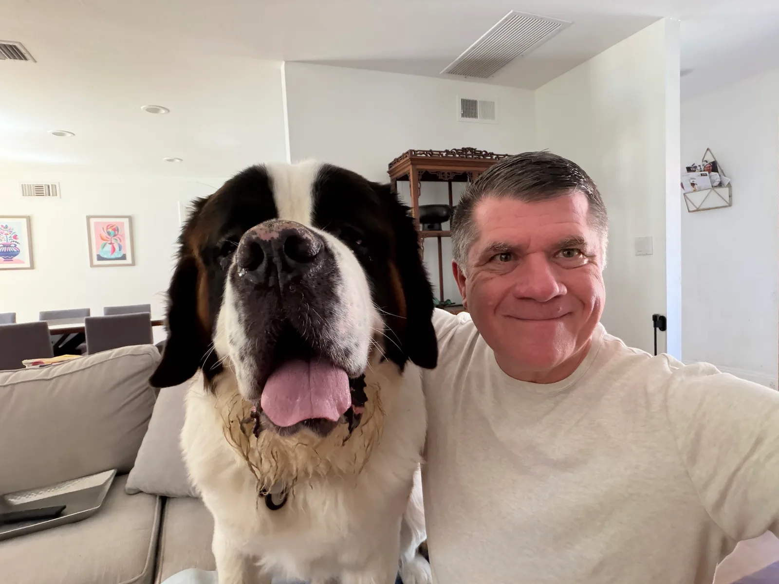 Steve Smith takes a close selfie on a living room couch with his arm around Magnus, his Saint Bernard, whose head fills the left half of the frame with his tongue out.