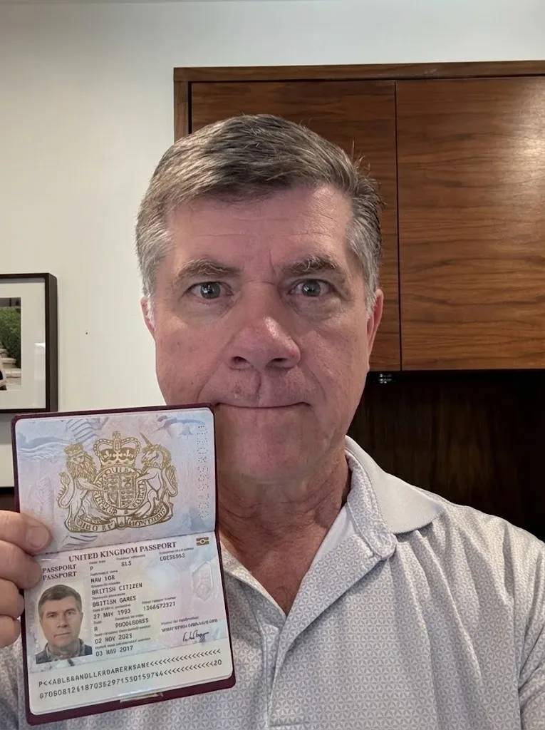 Man holding an open United Kingdom passport toward the camera in an indoor setting.