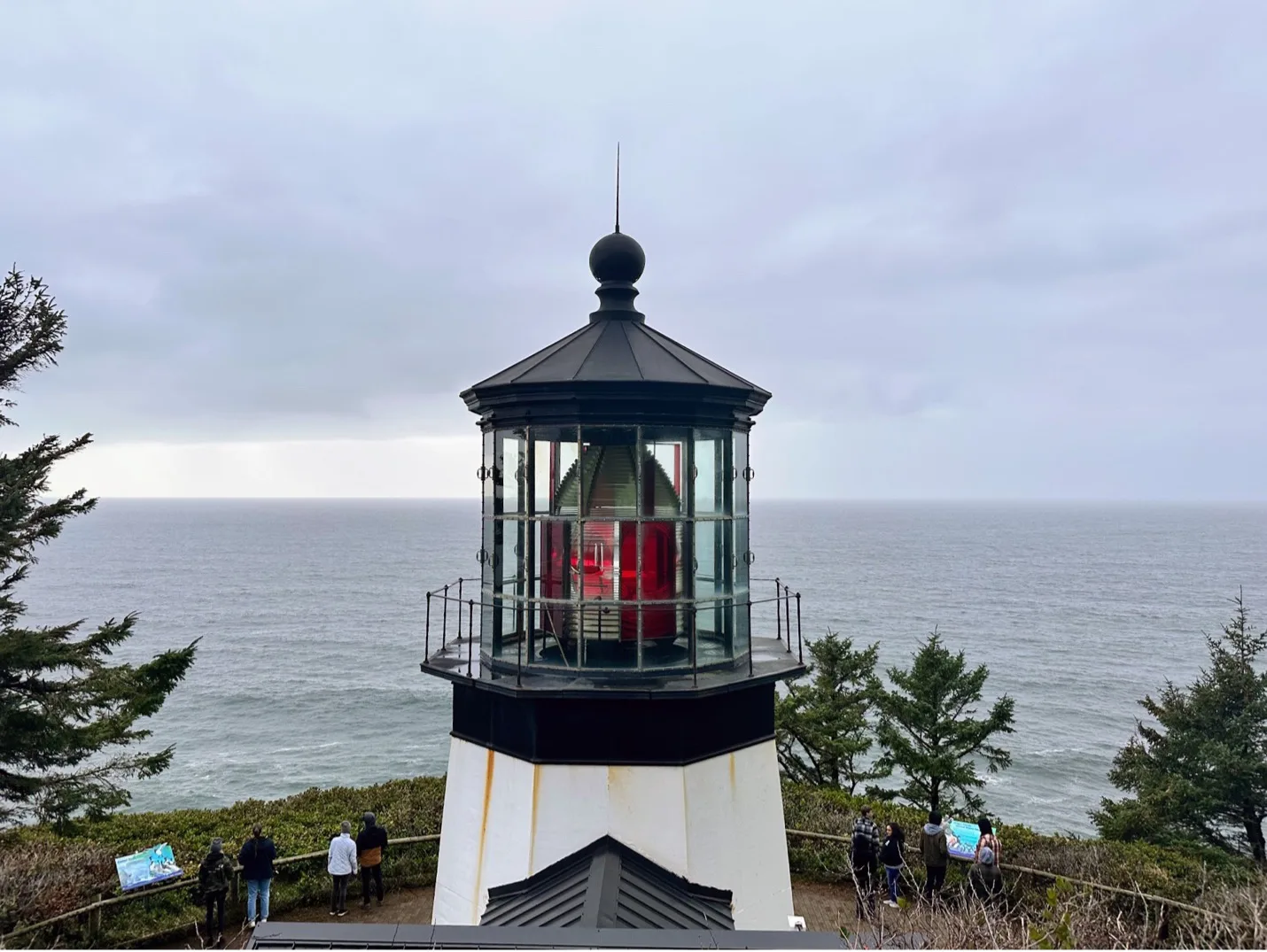 White lighthouse with a black dome and red lamp overlooking a gray ocean under cloudy sky.